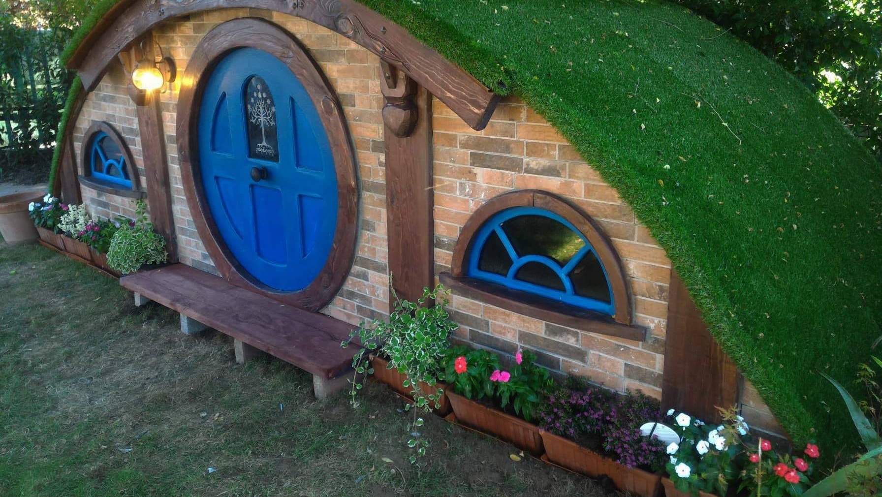 Casetta Hobbit in giardino con porta rotonda blu e copertura verde